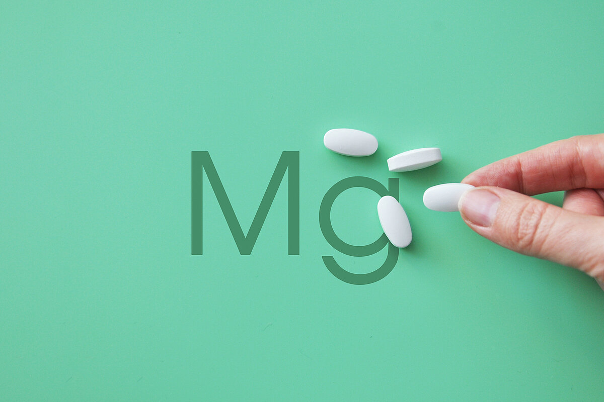 Magnesiumtabletten in einem Holzlöffel auf hellem Hintergrund