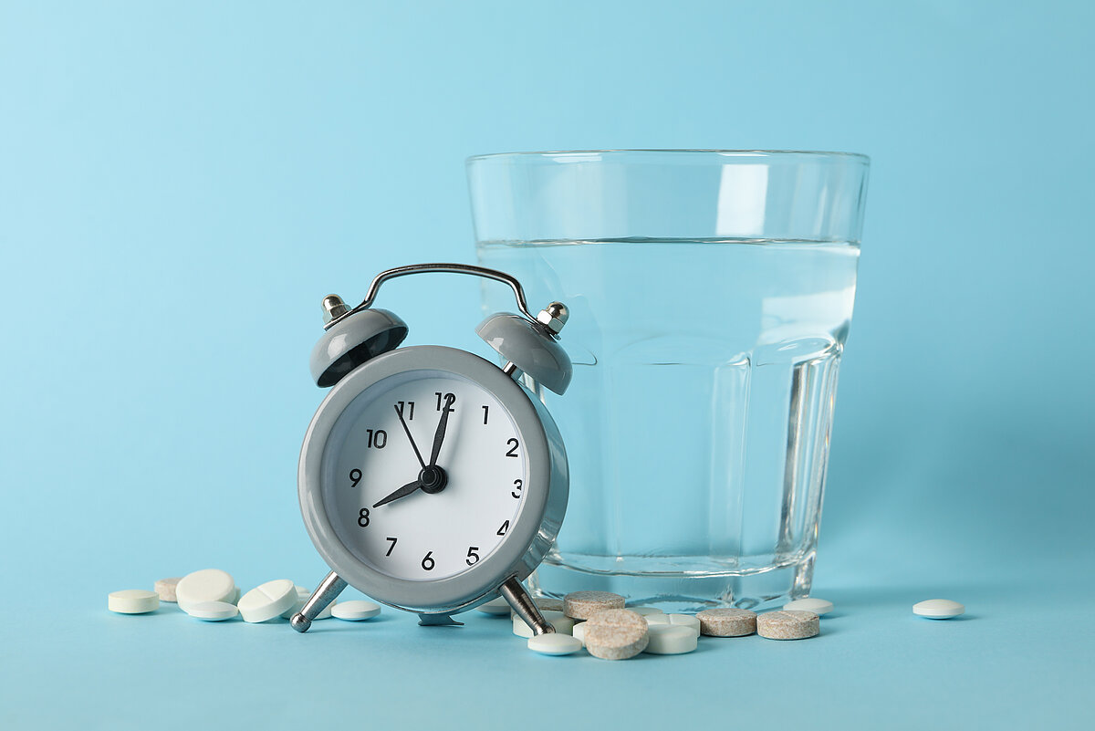 Wecker, Glas Wasser und Tabletten als Symbol für eine Einnahmeroutine